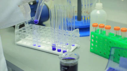 年轻女性实验室技术员检查圆锥形玻璃锥形瓶充满绿色的液体溶液进行化学试验时。实验室工作人员检查一个长颈瓶试剂。年轻的男性
